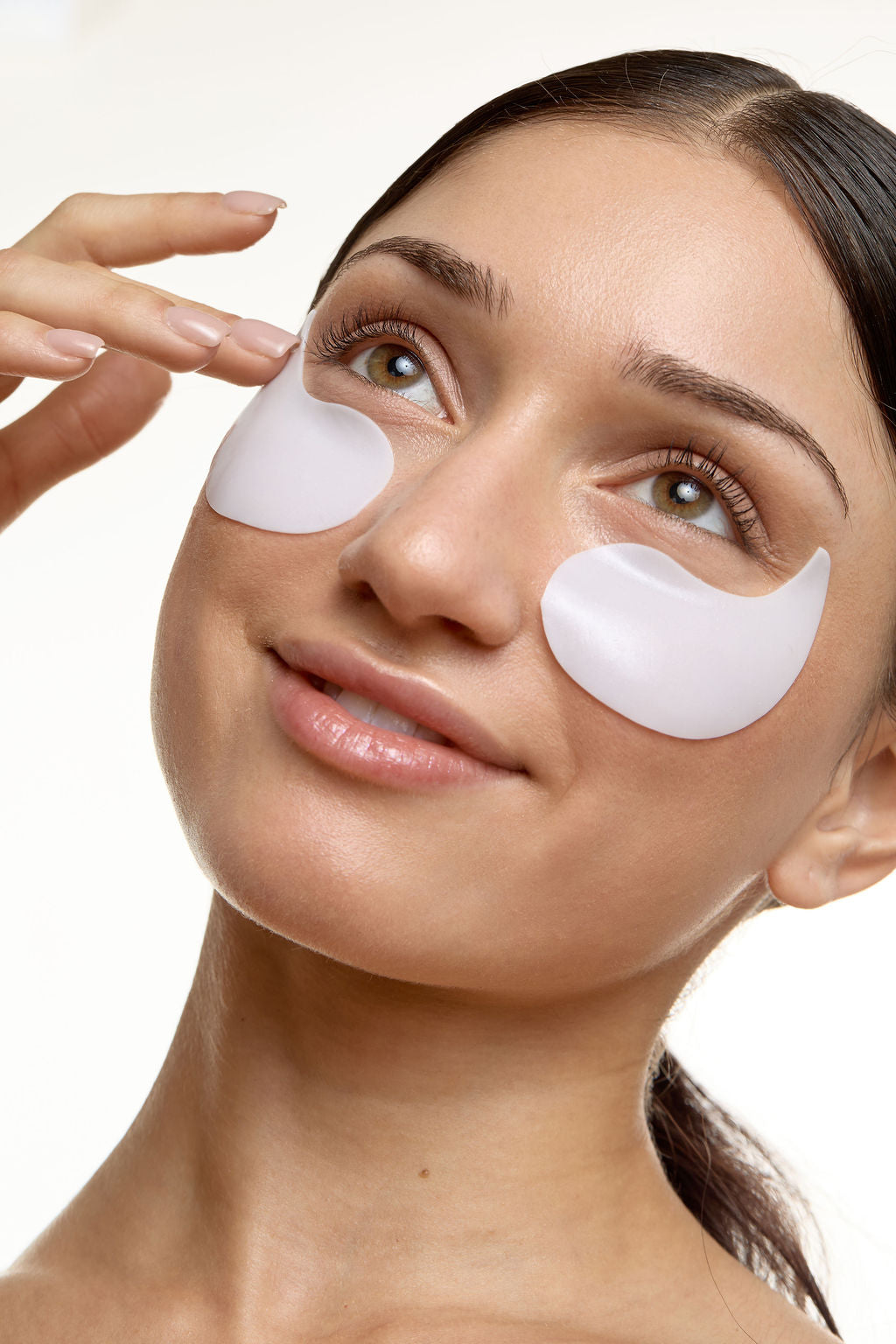 Woman applying eye patches on a white background