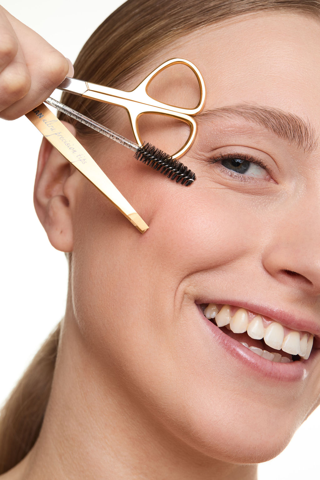 Woman using a gold eyebrow tools with a white background