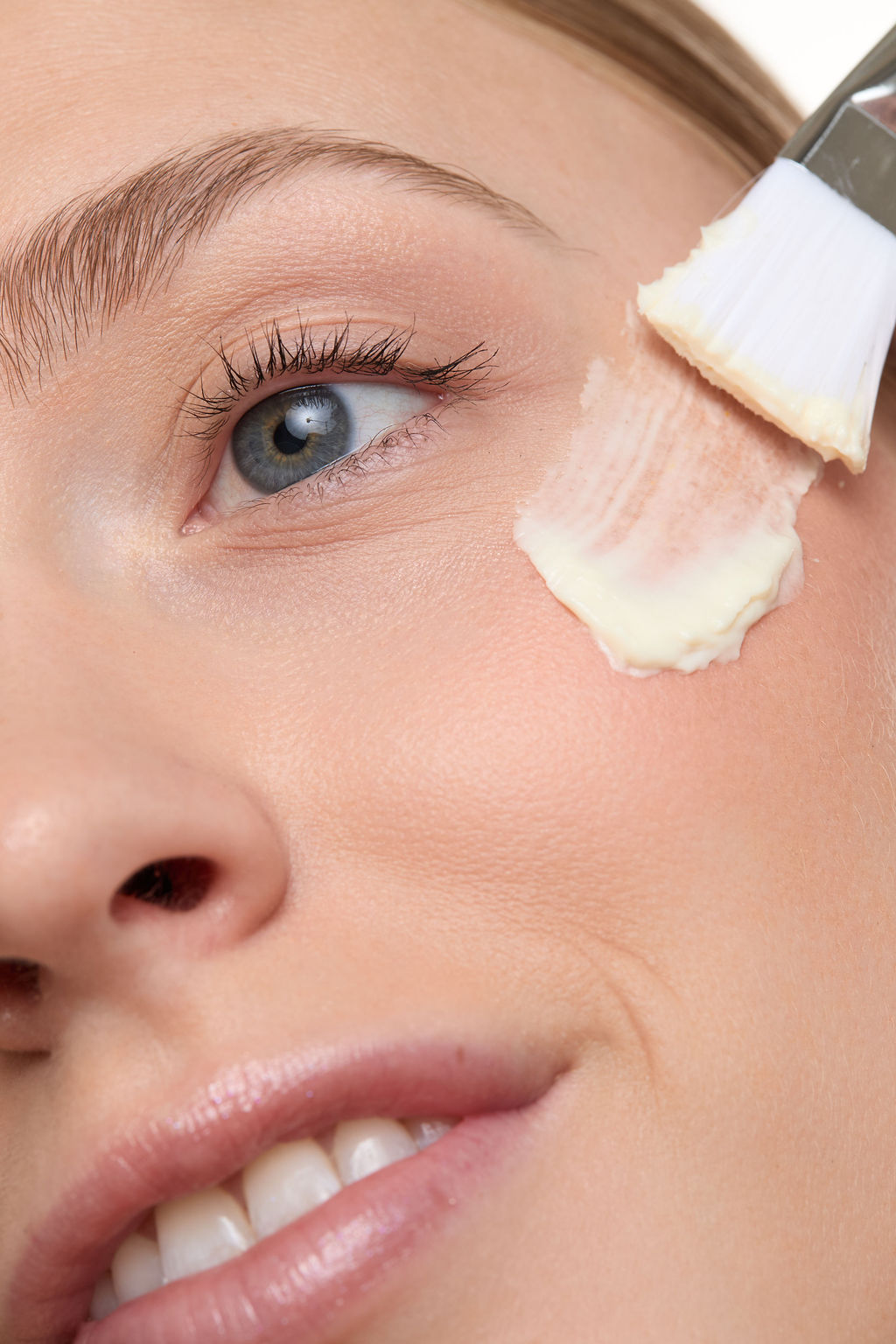 Close-up of a woman's face with a cosmetic brush applying cream to her cheek.