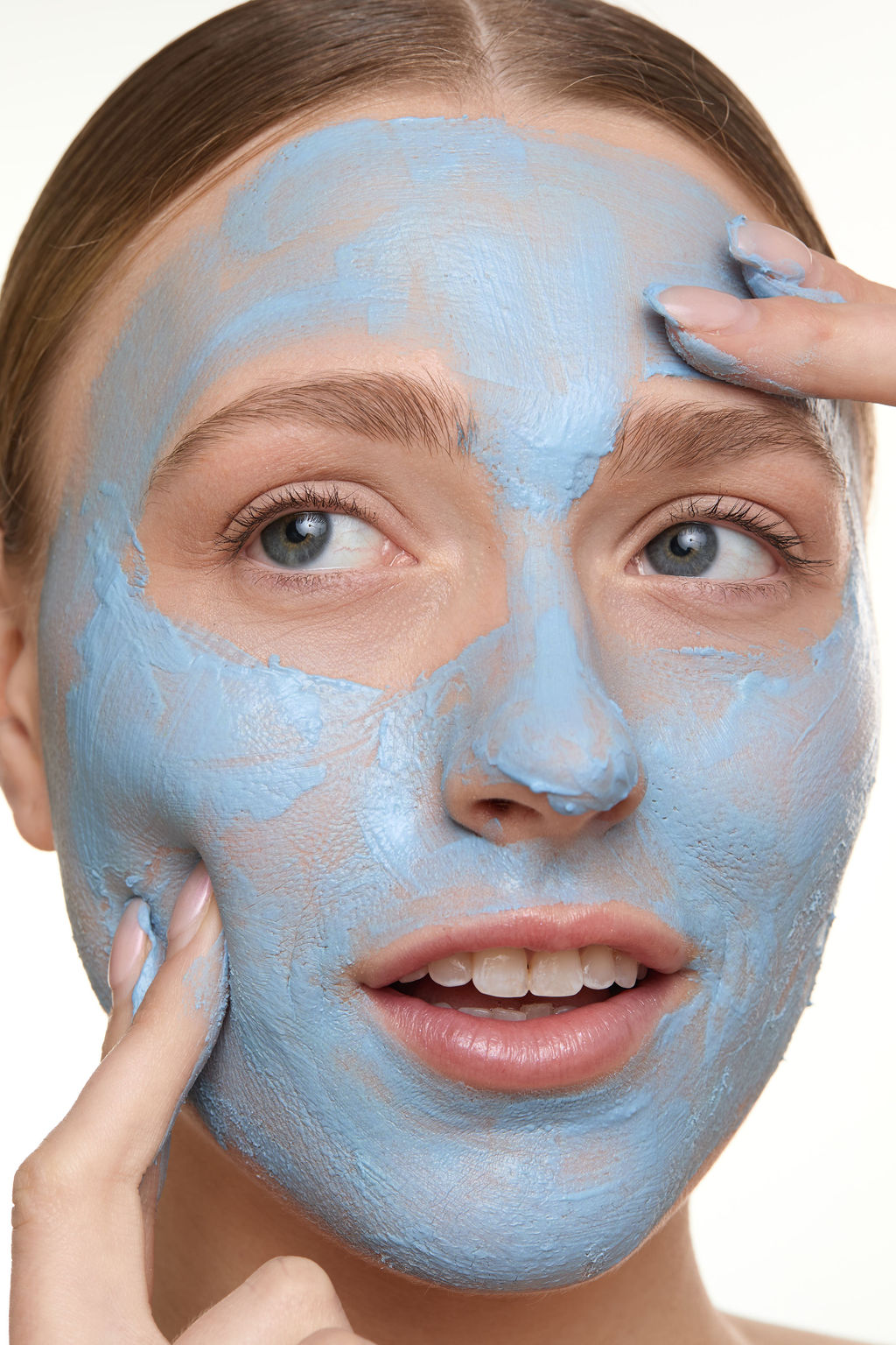 Woman applying a blue facial mask on her face against a white background