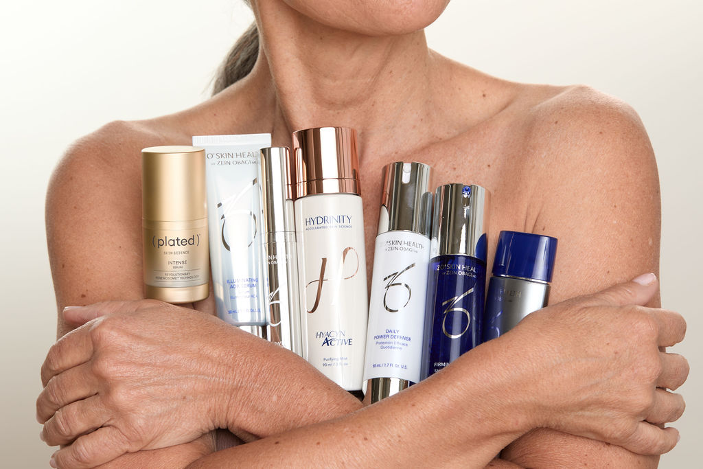 Woman holding a variety of skincare products against a neutral background