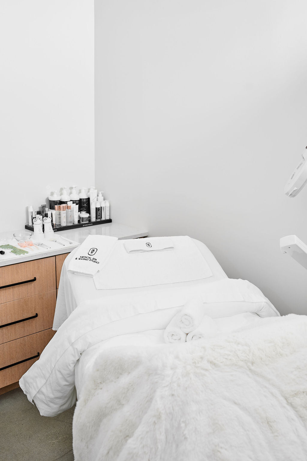 Treatment bed in a clinical setting with white sheets and a wooden cabinet.