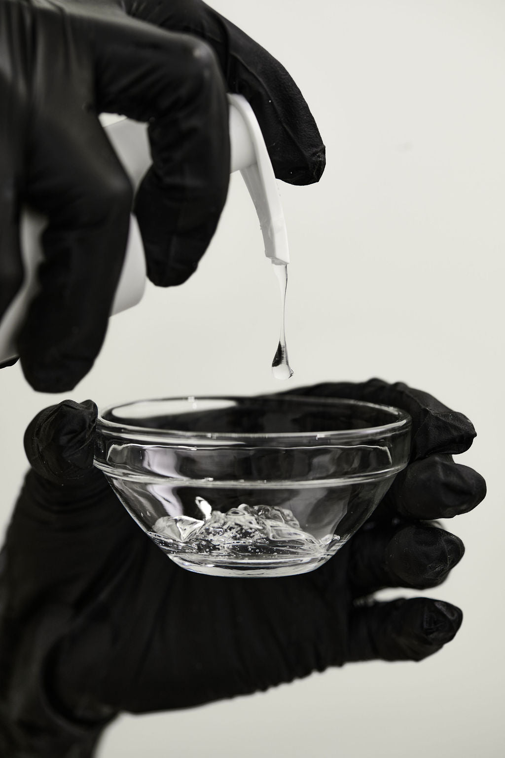 Person in black gloves holding a small glass bowl with a white background