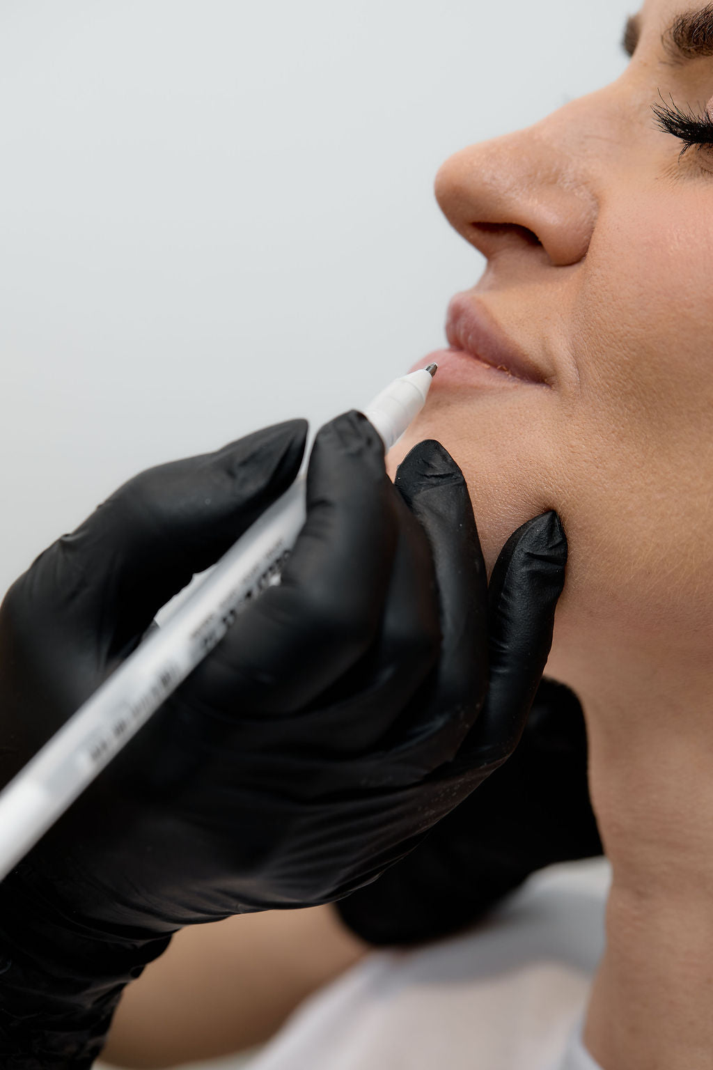 Person receiving pen markings on skin with a gloved hand on a neutral background